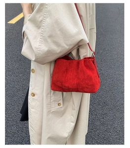 Dettaglio della borsa a secchiello in camoscio rosso con tracolla e trench beige