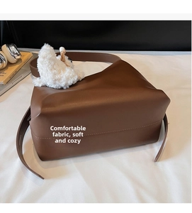 Detail of dark brown tote bag with white plush dog charm on a white bed background