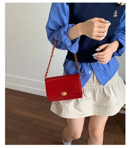 Detail of red leather square bag with gold oval twist lock and woven chain strap