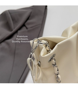 Detailed shot of silver eyelets and leather-woven chain strap on a cream shoulder bag