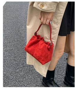 Chic red suede handbag with pleated design and metal buckle detail held by a model