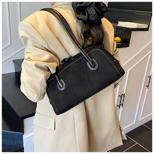Detail of black suede shoulder bag with white contrast stitching on model's beige suit