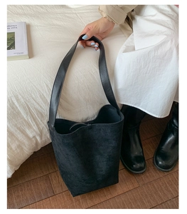 Detail of minimalist black frosted suede bucket bag with wide leather shoulder strap