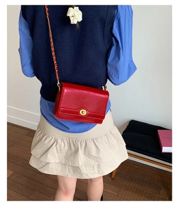 Detail of red crossbody bag with gold ring lock on a model in a stylish outfit