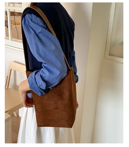 Close-up of deep brown suede bucket bag worn over shoulder with minimalist retro design