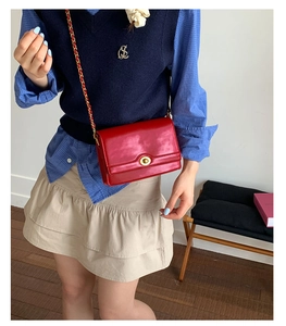 Detail of red patent leather crossbody bag featuring a golden twist-lock and chain strap