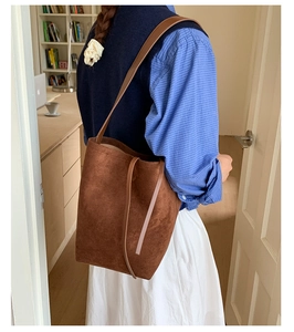 Detail of a brown suede bucket bag worn over the shoulder in a cozy interior setting