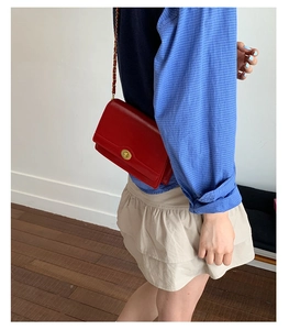 Close-up of red leather crossbody bag with golden chain and metallic twist lock