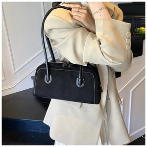 Detail of black suede baguette bag with contrast stitching held by a model in beige suit