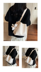 Detail of creamy white bucket bag featuring a wide strap and cute plush puppy charm