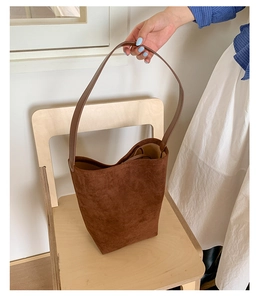 Detailed view of deep brown frosted leather bucket bag on a light wood chair