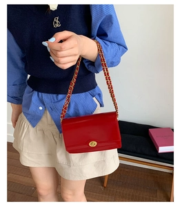 Detail of red patent leather crossbody bag with gold chain strap and oval twist lock