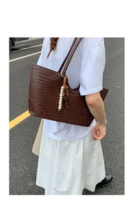 Detail of dark brown woven tote bag with beaded tassel charm on a model outdoors