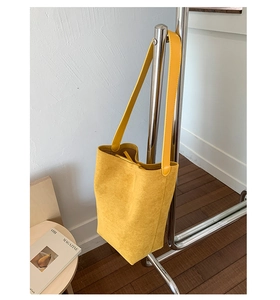 Detail of a large yellow suede tote bag hanging on a rack showing matte texture