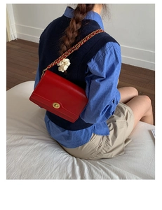 Detail of red leather crossbody bag with gold chain strap and floral charm accessory