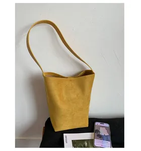 Detail of ginger yellow suede bucket bag with wide shoulder strap and square base design
