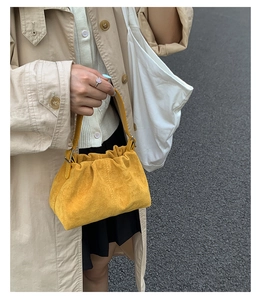 Detail of bright yellow suede cloud bag featuring soft pleated texture and top handle