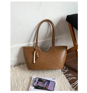 Detailed close-up of brown leather woven tote bag featuring decorative wooden bead charm