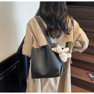 Detail view of a black leather bucket bag with a plush charm on a model in beige trench coat