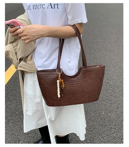 Detail of dark brown woven tote bag featuring artisan texture and ethnic wood bead charm