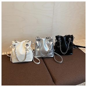 Chic drawstring bucket bags in white, silver, and black displayed on a leather bench