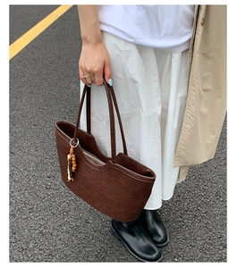 Detail of dark brown woven tote bag with wooden bead charm and metal zipper closure