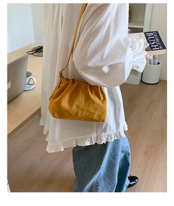 Detail of yellow suede cloud bag with soft pleated design and crossbody strap