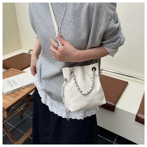 White leather bucket bag detail with silver chain handle and adjustable strap on a model