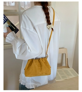 Dettaglio di una borsa a tracolla in camoscio giallo zenzero con camicetta bianca a balze