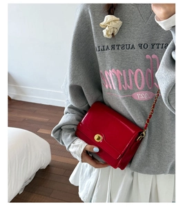 Red patent leather crossbody bag with gold chain strap shown worn by a model