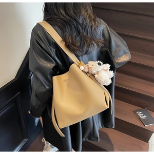 Minimalist beige bucket bag with plush bear charm shown in a lifestyle staircase setting