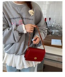 Detail of a red chain bag with gold twist lock worn over a grey sweatshirt