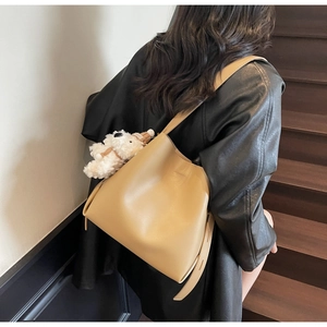 Close-up of beige leather bucket bag with cute white plush puppy charm on a model