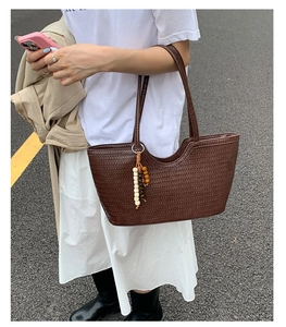 Detail of dark brown woven tote bag with smooth texture and decorative wooden bead tassel
