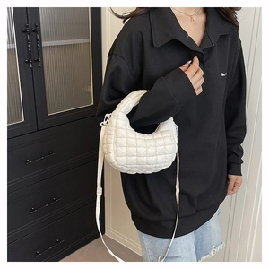 Detailed view of a white quilted dumpling bag worn by a model in a minimalist setting