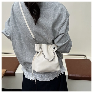 Detail of cream leather bucket bag featuring silver chain handle and drawstring closure