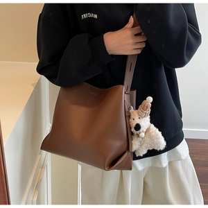 Detail view of a large brown leather bucket bag with a cute white plush puppy charm