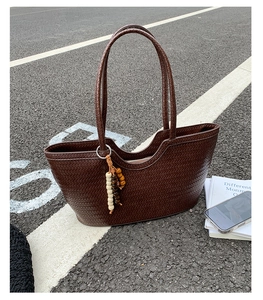 Close-up of woven dark brown tote bag with leather texture and bead charm on asphalt