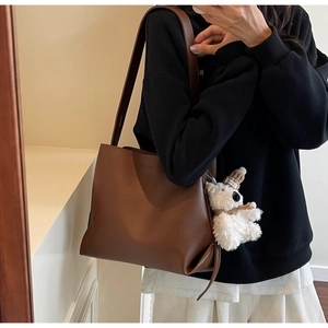 Detail view of brown leather bucket bag with plush bear charm and minimalist logo