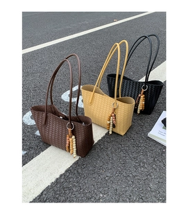 Detail of three woven tote bags in brown, beige, and black with colorful beaded charms