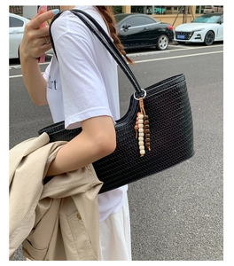 Detail of black woven tote bag with wooden bead charm accessory on a shoulder strap