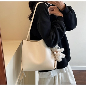 Detailed side view of off-white minimalist bucket bag with a cute white plush bear charm