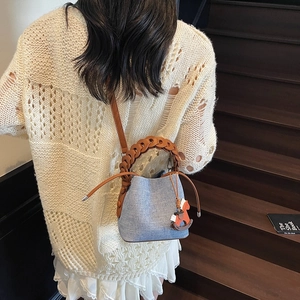Detail of light blue bucket bag with woven handle and horse charm on wooden stairs