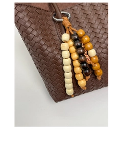 Detail of dark brown woven leather tote bag with wooden bead pendant and metal ring charm
