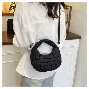 Detail of a black quilted dumpling bag with adjustable strap worn as a crossbody