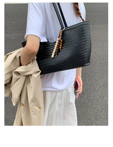 Detail of black woven tote bag with wooden bead charm worn as a shoulder bag