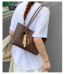 Detail of dark brown woven tote bag featuring a boho wood bead tassel and long straps