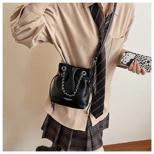 Detail view of a black leather bucket bag with silver chain and drawstring closure