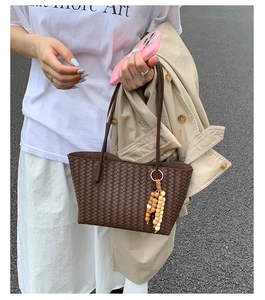 Detailed texture of brown woven tote bag with wooden bead charm in a street style setting