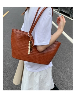 Detail of a brown woven tote bag featuring a multi-colored beaded tassel and metal ring